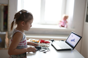 Kid constructs a robot from designer using laptop