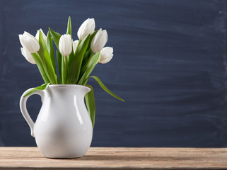 Bouquet of tulips in a oldfashioned rustic vase pot. Light colour flowers in white jug on a blur background.