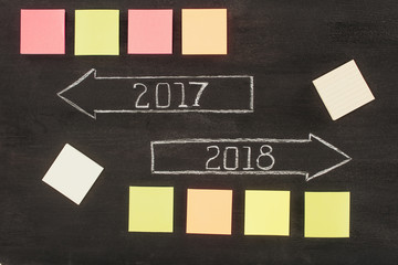 top view of arranged empty sticky notes and arrows with 2017, 2018 year signs on dark wooden surface