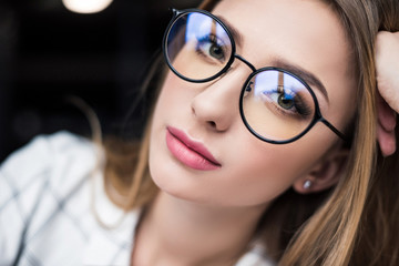 close-up portrait of beautiful young woman in eyeglasses looking at camera