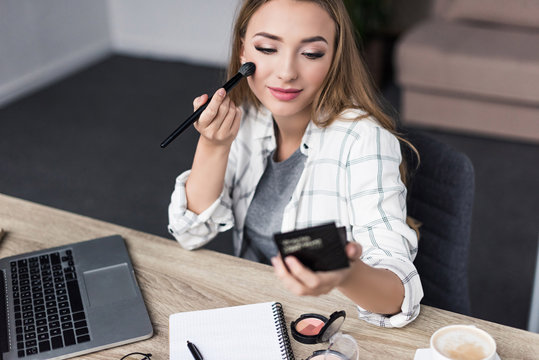 attractive young woman doing makeup at workplace and looking at mirror