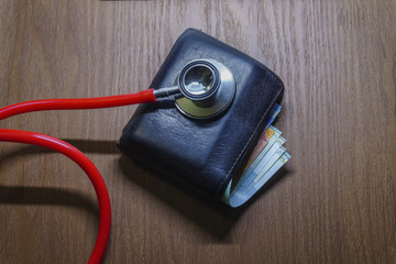 Conceptual image of diagnosing personal financial strength. Stethoscope on wallet with partly visible currency notes over brown surface. Selective focus; dimmed study lamp.