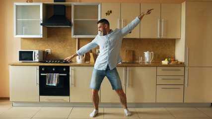 Handsome young funny man dancing in kitchen at home in the morning and have fun on holidays