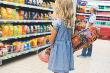 child with skateboard standing in supermarket with shelves behind