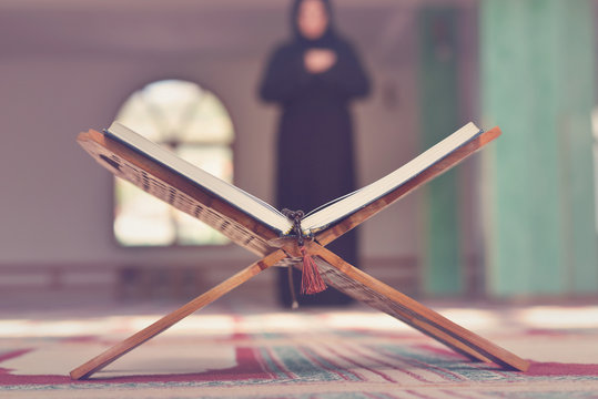 An open Holy quran with wood stand with praying people in background