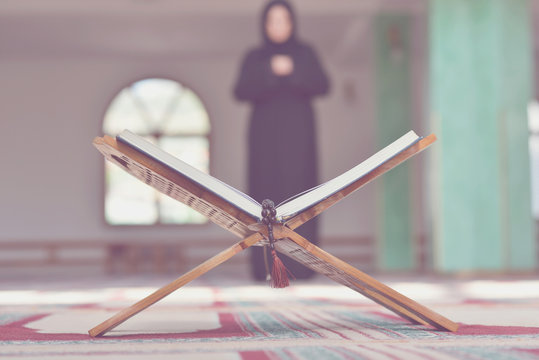 An open Holy quran with wood stand with praying people in background