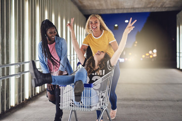 Young female friends playing with a shopping cart at night