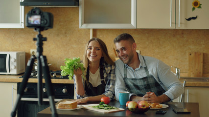 Young attractive couple shooting video food blog about cooking on dslr camera in the kitchen