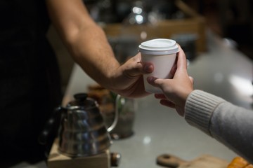 Mid section of waiter serving coffee to woman at counter