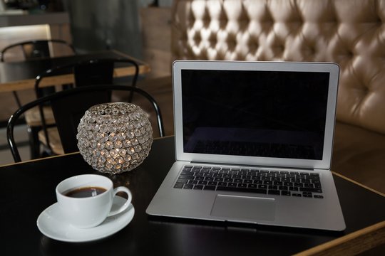 Close-up of coffee, laptop and lit candle on table