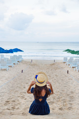 Fototapeta na wymiar Beautiful girl in a hat sits on a beach.