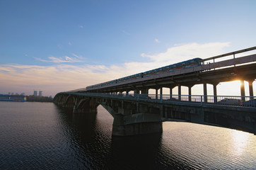 Picturesque view over the Metro (Subway) Bridge over the Dnipro river in Kyiv, Ukraine. Metro train are moving along the bridge. Sunrise at winter morning