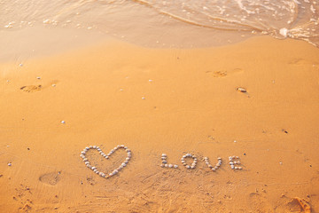 On the sand shells lined with heart and the word love.