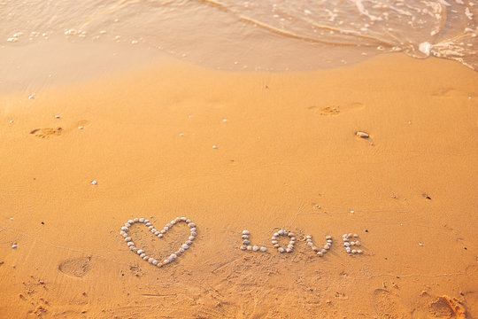 On the sand shells lined with heart and the word love.