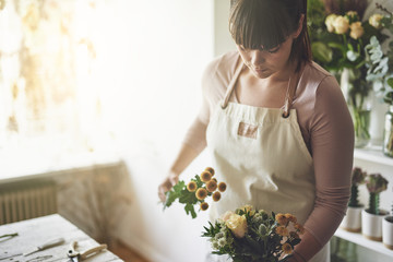 Young florist making a bouquet in her flower shop - obrazy, fototapety, plakaty