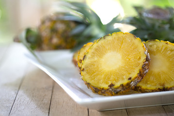 Pineapple slices with peel in white dish on wooden table, Blurred and selective focus and space for message..