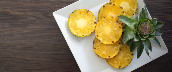 Pineapple slices with peel in white dish on wooden background