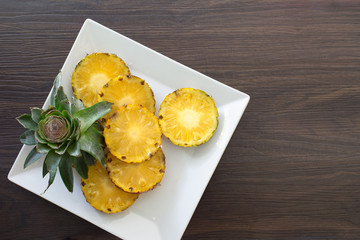 Pineapple slices with peel in white dish on wooden background