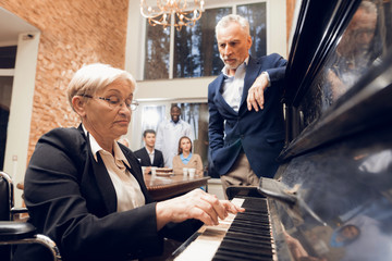 An elderly woman plays the piano at a nursing home.