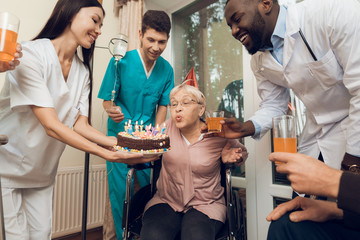 A group of young and old people in a nursing home congratulate an elderly woman on her birthday.