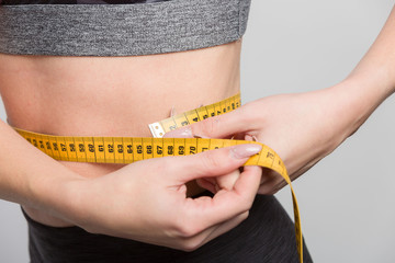 Nahaufnahme einer jungen Frau, die sich den Taillenumfang mit einem Massband misst