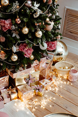 set of gold and silver gift boxes under a Christmas tree. Gifts lie on the wooden floor decorated with the shining garland.