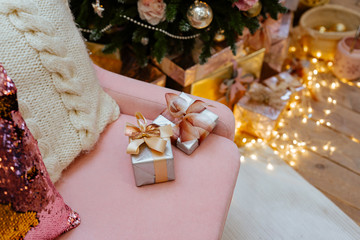 two small beautiful gift boxes of silver color with a graceful tape lie on a pink sofa against the background of a Christmas fir-tree.