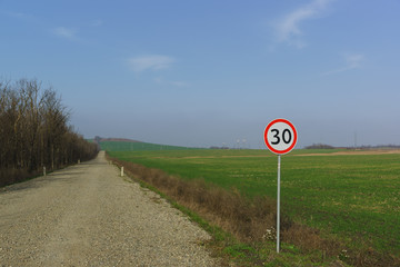 Car sign speed limit 30 kilometers per hour is on the side of the dirt road along the fields of green shoots