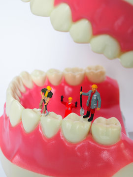Miniature worker on plastic teeth of removable denture. Dental health concept.