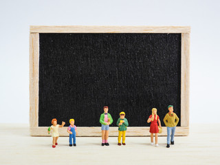 Miniature children standing in front of a blackboard on wooden background. Back to school concept.