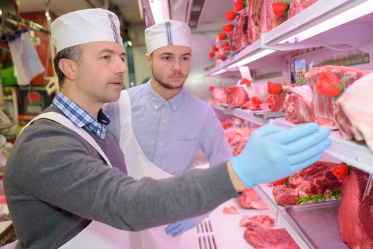 butcher teaching a young one how to sell meat