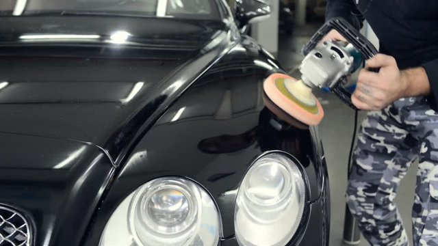 A man polishes a black car with a polisher