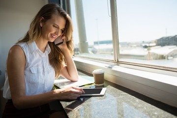 Businesswoman talking on mobile phone while using digital tablet