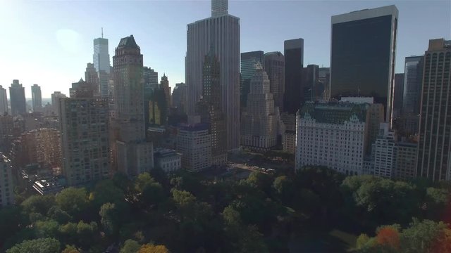 Aerial real time shot, camera is flying above Central Park moving away from the intersection between West 95th Street and Fifth Avenue in New York. Camera is moving backwards filming the crossroad.