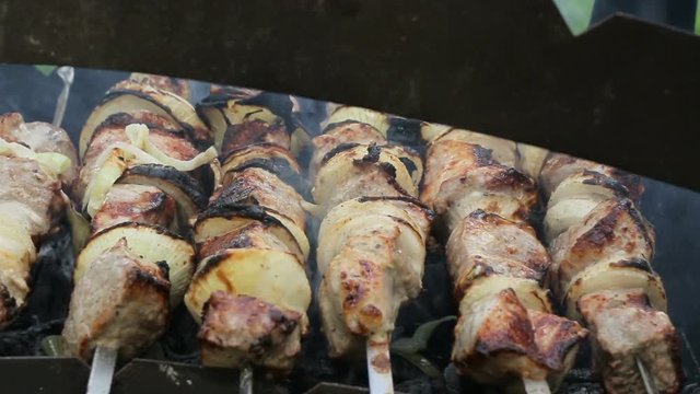 The man turns the skewers with meat on the grill. Shish kebab in the nature, video footage of a barbecue. With camera movement on the slider