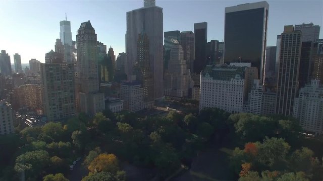 Aerial real time shot, camera is flying above Central Park and approaching to the intersection between West 95th Street and Fifth Avenue in New York City. Camera is moving forward filming skyscrapers.
