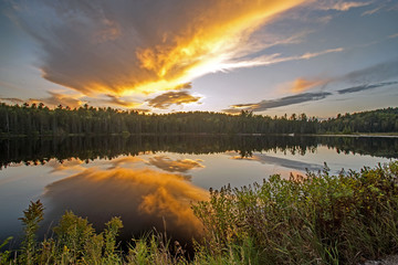 Fototapeta na wymiar Large orange cloud hangs over a small lake