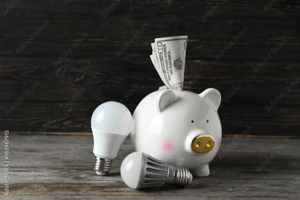 Canvas Prints Piggy bank with money and light bulbs on wooden background