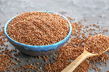 Bowl and spoon with raw buckwheat on table