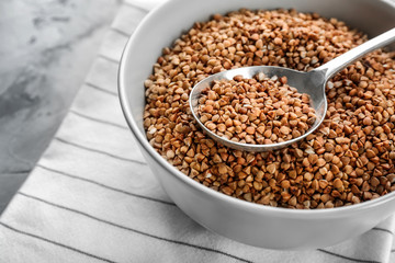 Bowl and spoon with raw buckwheat and spoon on table