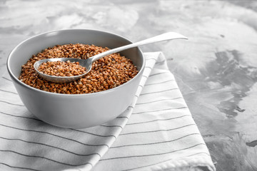 Bowl and spoon with raw buckwheat and spoon on table