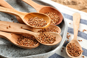 Wooden spoons with raw buckwheat on table