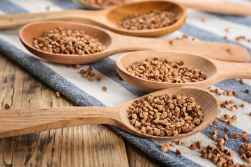 Wooden spoons with raw buckwheat on table