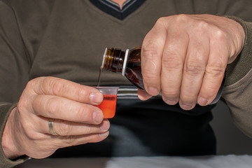 An elderly man is administering liquid medicine. Focus on the hand and bottle. concept: healthcare, people and medicine