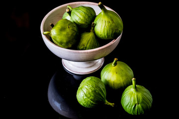 Green figs in a rustic, footed bowl with dark background