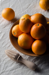Oranges in a wooden bowl on a white linen tablecloth.