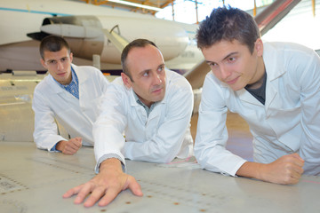 Students in aircraft hangar looking at plan of fuselage - obrazy, fototapety, plakaty