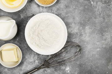 Ingredients for pastries - flour, eggs, butter, milk, sugar on a gray background. Top view, copy space. Food background