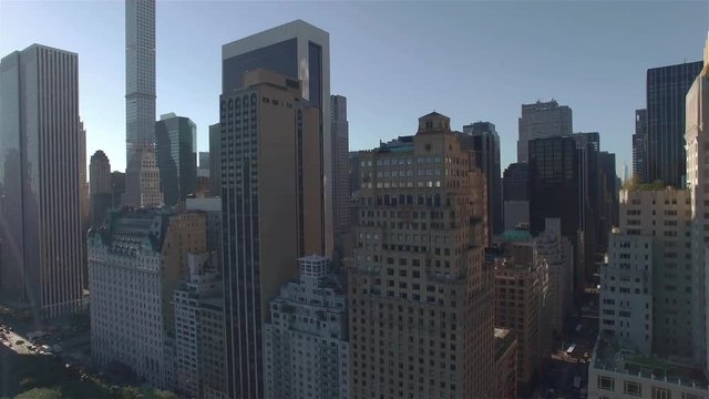 Aerial real time shot, camera is flying above Central Park along West 95th Street, reaching the 6th Avenue, the camera changes the direction and flying backwards away from the intersection.