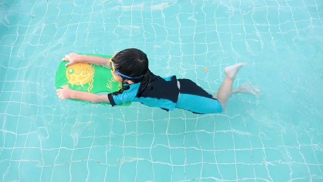 A boy is learning to swim to improve his swimming skills in the swimming pool with goggles and swimming foam for floating